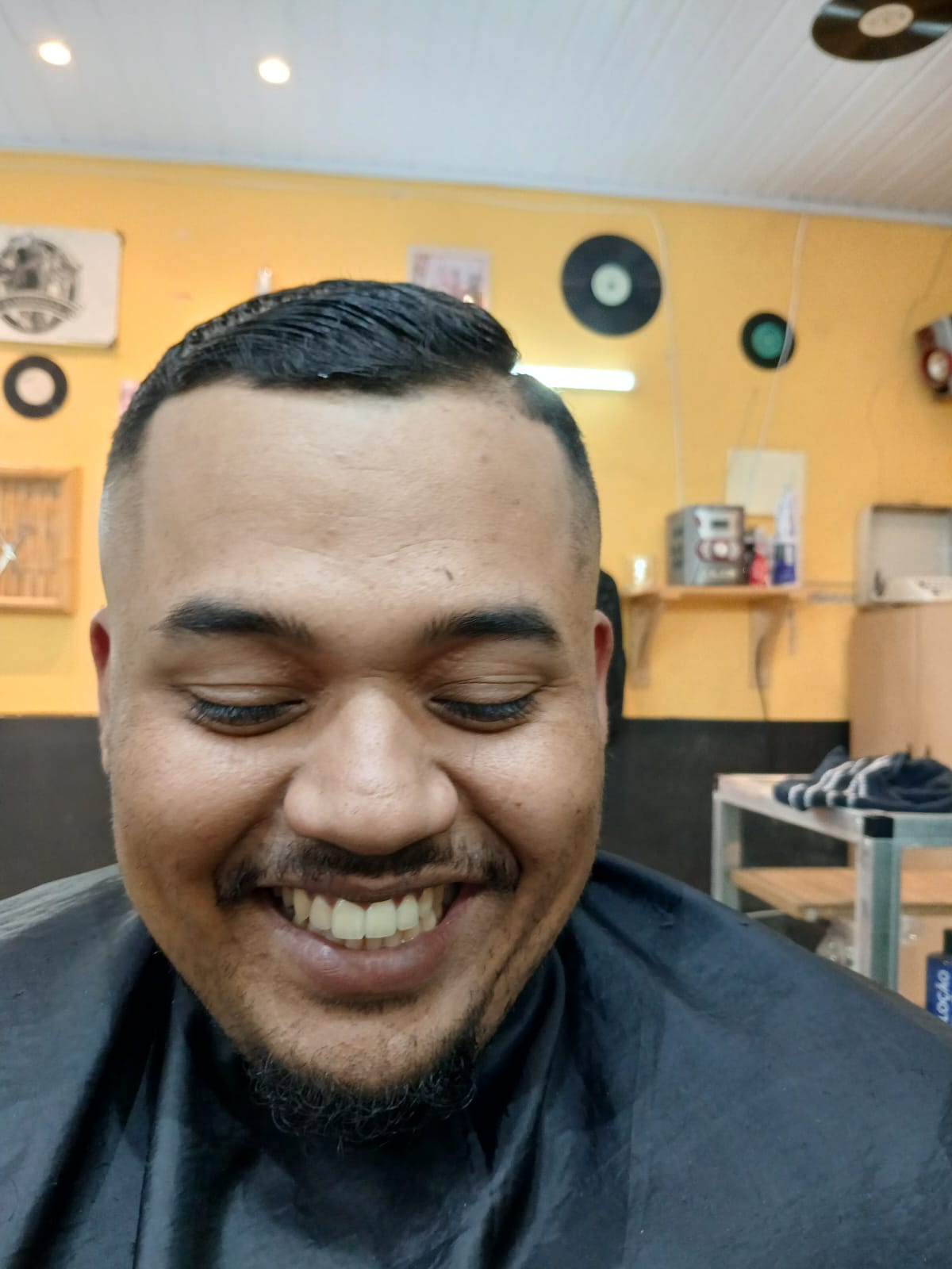 cliente sorrindo com capa preta exibindo corte degradê recém-feito no interior da barbearia
