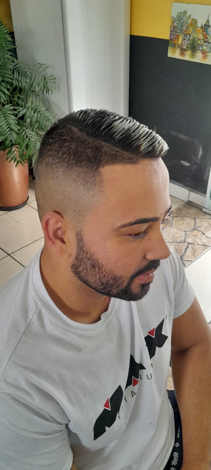 corte degradê na lateral com topo penteado para trás e barba alinhada